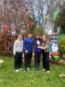Four people smiling and standing in a yard with bunting.